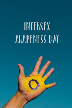 Genç bir insanın avucundaki cinsiyetler arası bayrağın yakın çekimi ve yukarıdaki mavi gökyüzünde cinsiyetler arası farkındalık günü