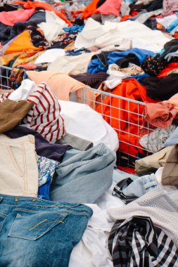 Kotlar, gömlekler ve birçok kumaş ve güneş gözlükleriyle dolu diğer giysiler kalabalık bir açık hava pazarında gün ışığında büyük tel kutulara tıkıştırılır.
