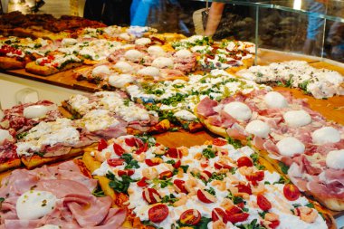İtalyan pizzası al taglio mozzarella, mortadella, karides, domates ve diğer taze malzemeler İtalya 'daki bir pizzacının cam tezgahında sergileniyor.