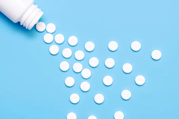 handful of white pills scattered on a blue background