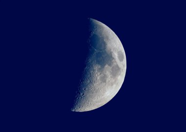 Astronomik bir teleskopla görülen ilk çeyrek ay, koyu mavi gökyüzü arkaplanı