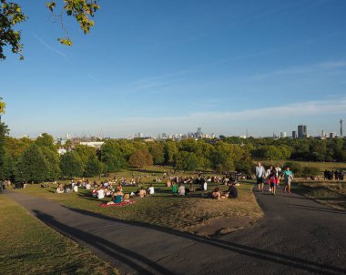 LONDON, İngiltere - CIRCA SEPTEMBER 2019: Regent 's Park' ın kuzeyindeki Primrose Hill 'de insanlar gün batımında Londra ufuk çizgisine bakıyor