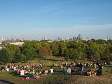 LONDON, İngiltere - CIRCA SEPTEMBER 2019: Regent 's Park' ın kuzeyindeki Primrose Hill 'de insanlar gün batımında Londra ufuk çizgisine bakıyor