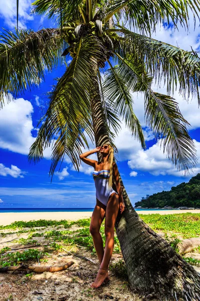 Beautiful woman in white bikini posing at the palm tree, Karon beach, Phuket, Thailand