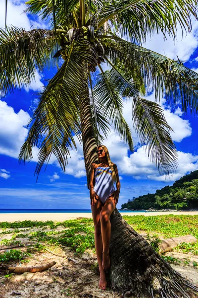 Beautiful woman in white bikini posing at the palm tree, Karon beach, Phuket, Thailand