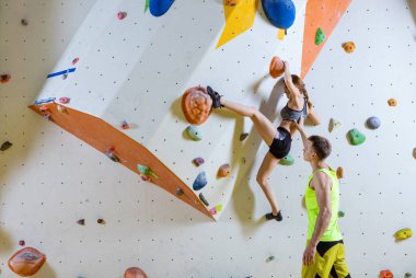 Spor tırmanış içinde kaya dağcılar. Genç kadın Bouldering sorun (yol), erkek eğitmen onu güvenliğini sağlama tırmanma.
