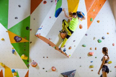Spor tırmanış içinde kaya dağcılar. Genç adam Bouldering sorun (yol), onu izlerken kız dağcı.