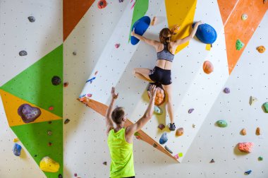 Spor tırmanış içinde kaya dağcılar. Genç kadın Bouldering sorun (yol), erkek eğitmen onu güvenliğini sağlama tırmanma.