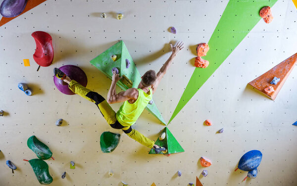 Young man climbing bouldering route, doing splits to reach next handhold. In indoor climbing gym.