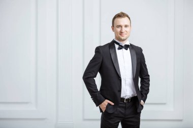 Gülümseyen ve kapalı kameraya bakarak smokin çekici genç adam