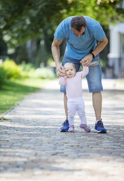 父亲支持小女儿 帮助她迈出第一步 爸爸和女儿在夏日公园散步 — 图库照片