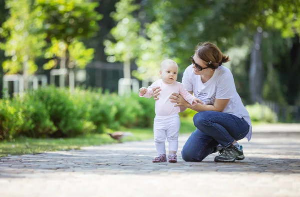 母の赤ん坊の娘をサポートし 彼女の作成の最初のステップを支援します ママと娘の夏の公園の中を歩く — ストック写真
