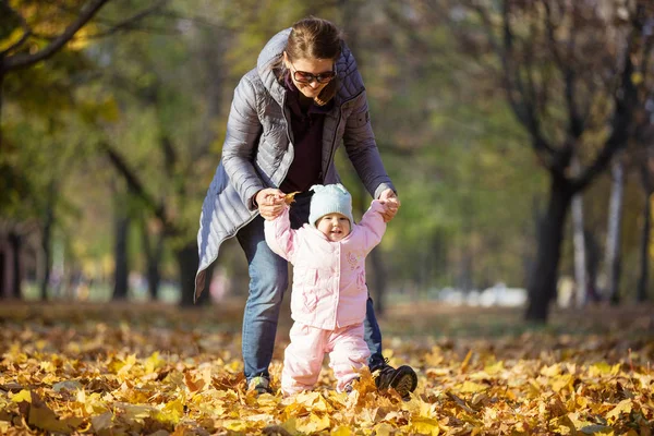 母亲支持小女儿 帮助她迈出第一步 妈妈和女儿在秋天的公园散步 — 图库照片