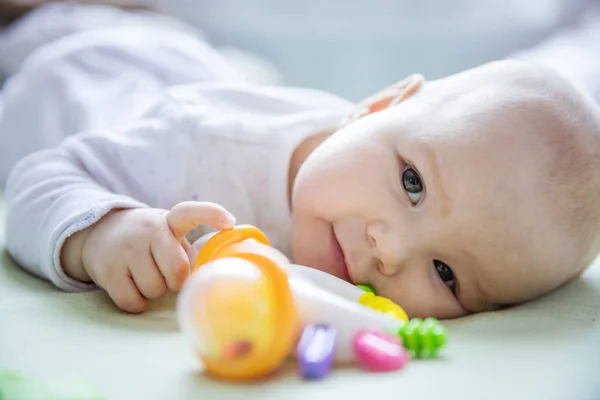 Cute baby girl playing with rattle while lying down on bed — Stock Photo, Image