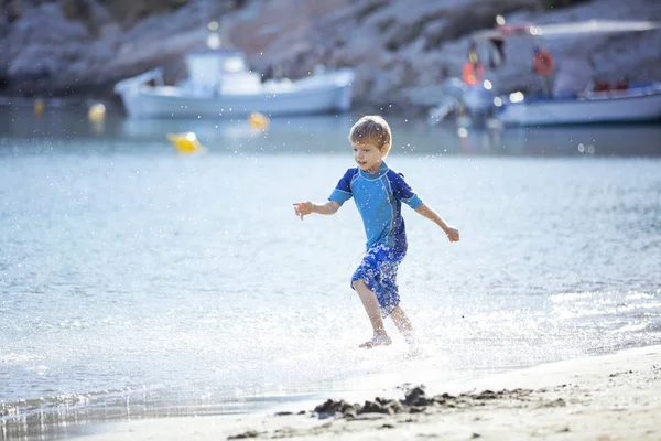 Glücklicher kleiner Junge läuft am Wasserrand entlang und macht Spritzer — Stockfoto