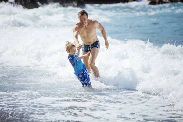 Father and son playing on the beach in rough water — Stock Photo, Image