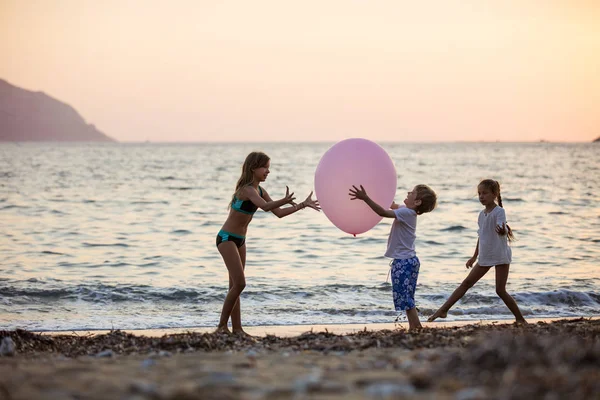 Children playing with huge pink balloon on beach at sunset — Stock Photo, Image