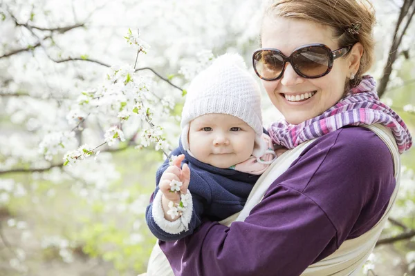 Young woman carrying her baby daughter outdoors in spring park — Stock Photo, Image