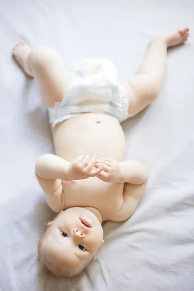 Menina bonito olhando para a câmera enquanto deitado na cama — Fotografia de Stock