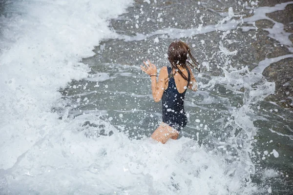 Молодая девушка прыгает в больших волнах с водой брызг вокруг — стоковое фото