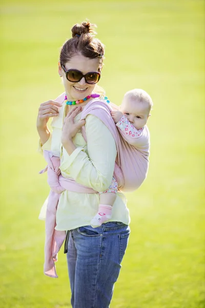 陽気な白人女性の背中に彼女の赤ん坊の娘を運ぶ — ストック写真