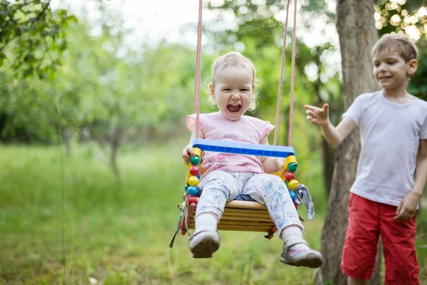 Joven chico empujando pequeño hermana en swing — Foto de Stock