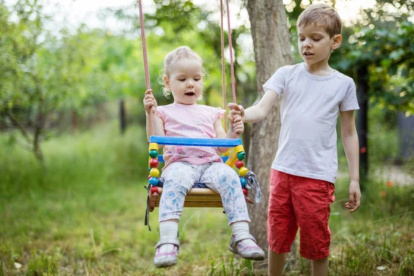 Junge schubst Kleinkind-Schwester auf Schaukel — Stockfoto