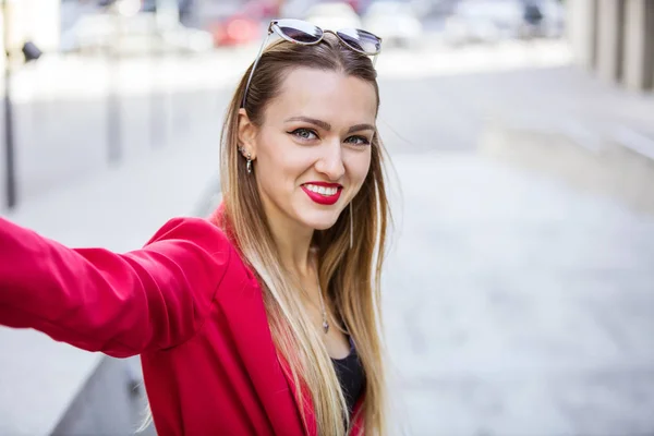 Piękna młoda kobieta w czerwonym garniturze robi selfie na zewnątrz — Zdjęcie stockowe