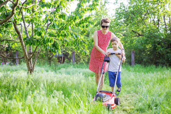 母亲和儿子在花园里用割草机割草 — 图库照片