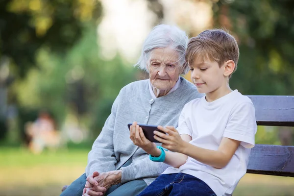 若い男の子と彼の曾祖母はスマートフォンでビデオを見ています スマートフォンを使って自撮り ビデオ通話をする モバイルインターネット 携帯電話でゲームをプレイ — ストック写真