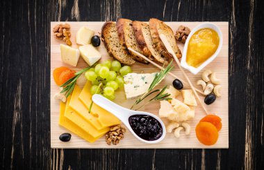 Peynir tabağı dilimlenmiş ekmek, üzüm, kurutulmuş kayısı, zeytin, reçel, bal ve ahşap arka planda fındık ile servis edilir.