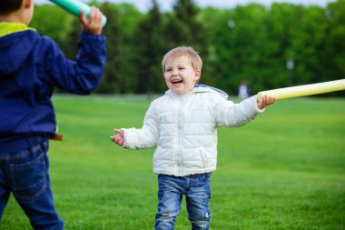 Oyuncak kılıçlarla oynayan ve parkta gülen iki kardeş.