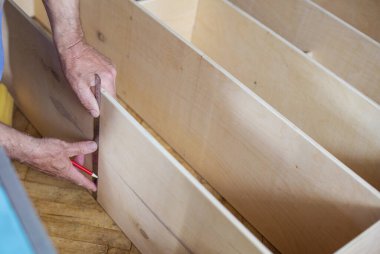 Ahşap rafı cetvelle ölçen olgun bir adam raf ünitesi yaparken, erkek elini kırpıyordu.