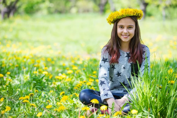 Słodkie Młoda Dziewczyna Noszenie Wieniec Mniszki Lekarskie Uśmiech Siedząc Trawie — Zdjęcie stockowe