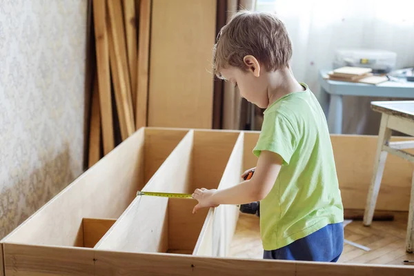 リールを使って本棚や棚の木棚を測定する少年 — ストック写真