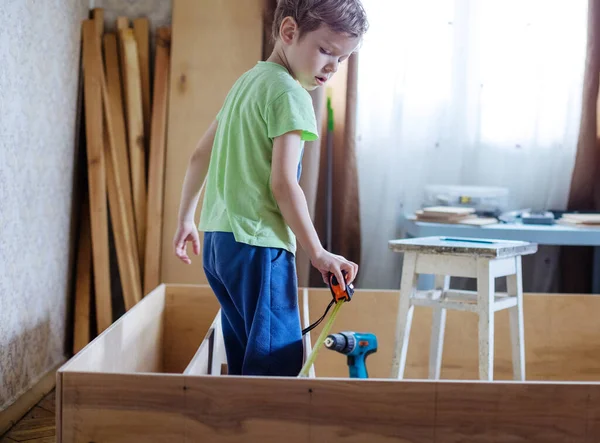 可爱的小男孩用卷轴测量木制书架或书架单位 — 图库照片