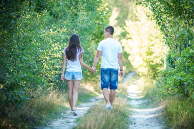 Genç çift yaz ormanlarında yürüyor ve el ele tutuşuyorlar.