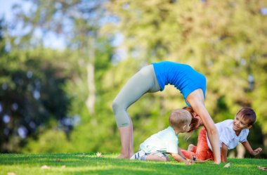 Yaz parkında çalışan genç bir kadın, yanında oynayan küçük oğullar.