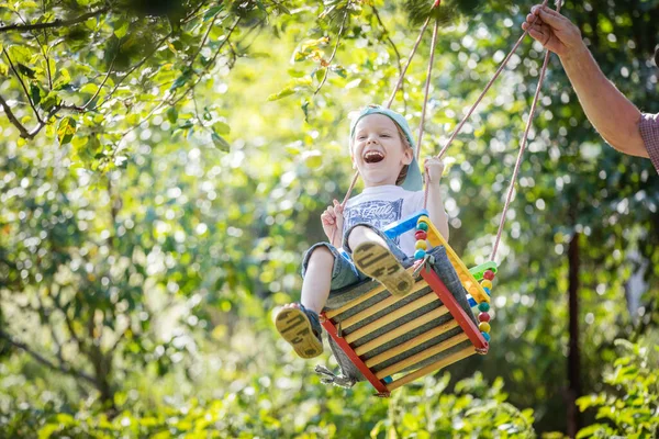 Senior Schubst Lachenden Enkel Auf Schaukel Garten — Stockfoto