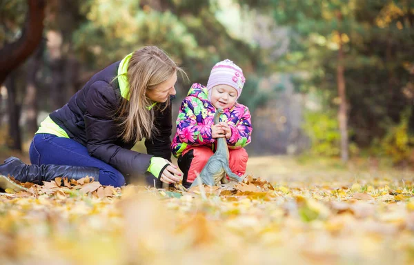 小女孩和妈妈在秋天的公园里玩玩具恐龙 — 图库照片