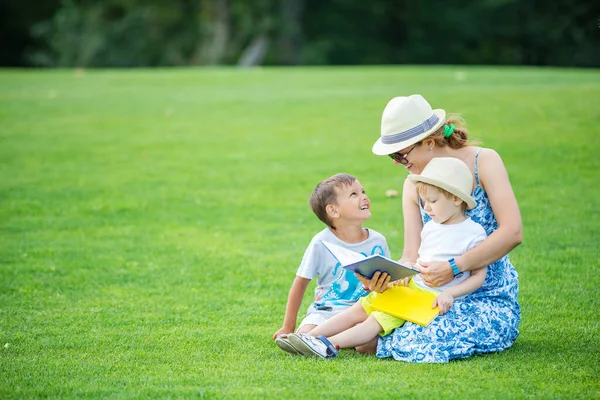 Młoda Matka Czyta Książki Dwóm Małym Synom Siedząc Trawie Parku — Zdjęcie stockowe