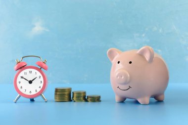 A small pink alarm clock and a piggy bank stand on a blue table. Between them are three stacks of coins of different heights. Beautiful bright photo. The symbol of the growth of money. clipart