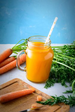 Yararlı veggie içki. Havuç suyu ve sebze alışılmadık bir mavi arka plan üzerinde bir kavanoz ile güzel kompozisyon.