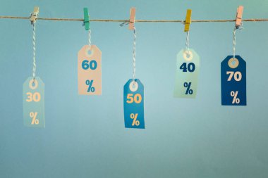 Etiketleri clothespins ile bağlı bir ip dayan. İskonto değerleri onları, elli, otuz, % 60 üzerinde yazılır. Mavi bir arka plan resmi.