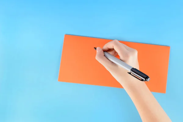 På en blå bakgrund ligger ett orange kuvert. Handen på en ung flicka undertecknar det. — Stockfoto