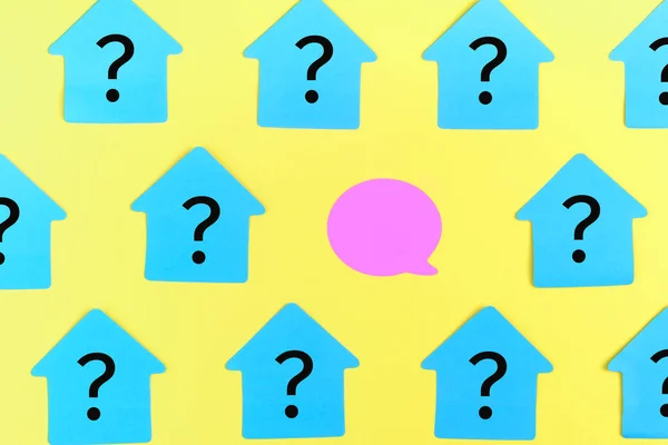 Бирюзовые наклейки в виде дома, с вопросительными знаками. В центре пустой фиолетовой наклейки в виде пузыря. Фото на ярко-желтом фоне . — стоковое фото