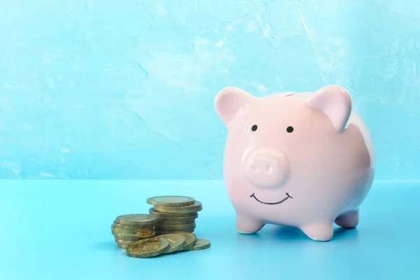 Piggy bank on a light turquoise background. Near to three stacks of coins. The symbol is the accumulation and conservation of money. — Stock Photo, Image