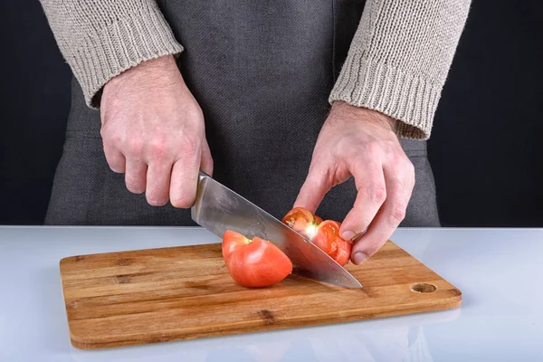 Mannen skär en tomat i två halvor med en kniv. Ett vackert foto av tillagningen. — Stockfoto