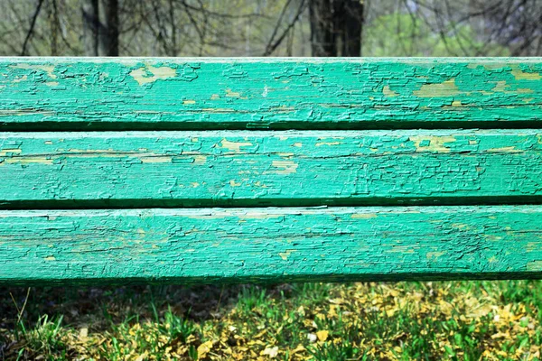 Viejas tablas de madera con pintura verde agrietada. En el fondo, los árboles y la hierba están borrosos . — Foto de Stock