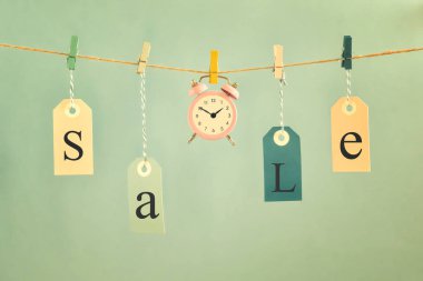 Açık mavi renkli ip asmak üzerinde üzerinde Satılık etiketlerini etiketli. Küçük pembe çalar saat merkezidir. Kavram, satış için zaman.